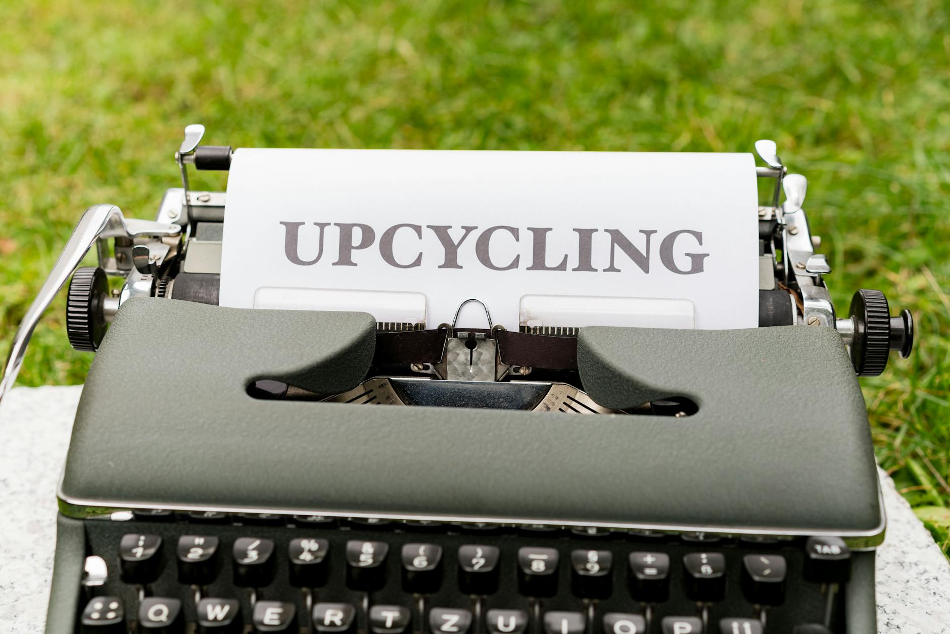 A retro typewriter displaying the word 'upcycling' outdoors on grassy ground.