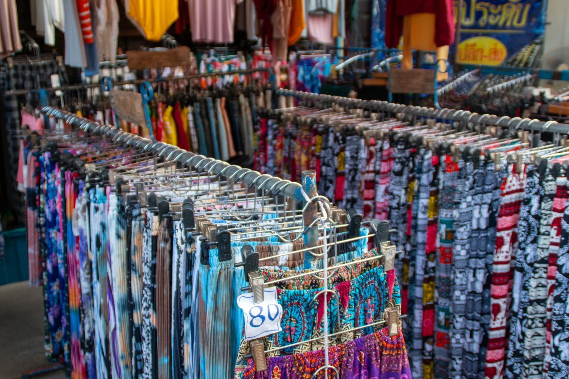 Price Comparison: Thrift Store vs. Retail - Vibrant array of clothing on racks in an outdoor market setting.