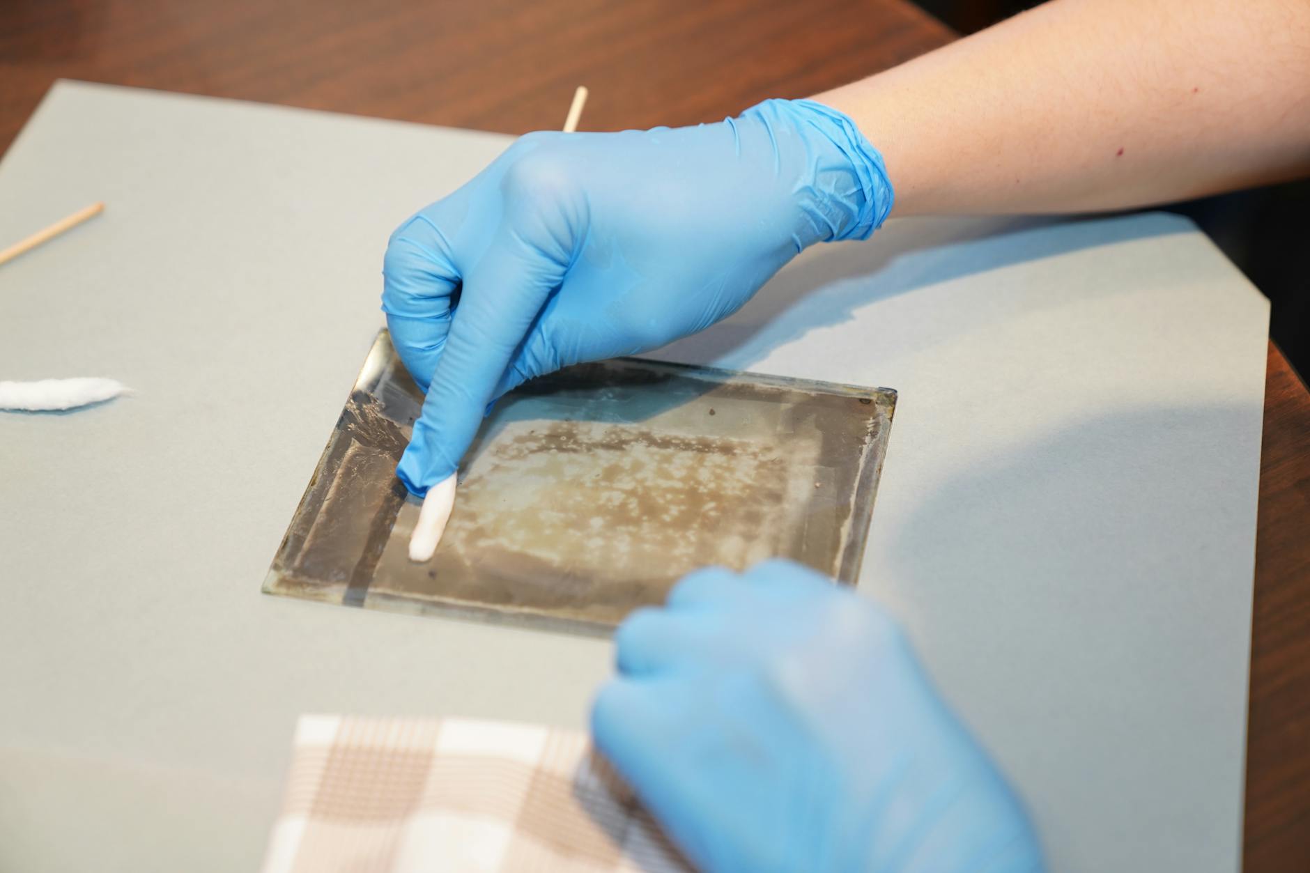 Restoration: How to Clean Your Finds - Hands in gloves carefully restoring vintage artwork on glass using cleaning tool